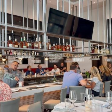 Guests seated at the long bar under overhead glass racks at Rosebud Steakhouse in St. Charles