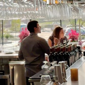 Bartender serving guests at the bar of Rosebud Steakhouse in St. Charles, beneath hanging wine glasses